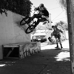 black and white photograph of a man doing a trick on his bike while another person watches