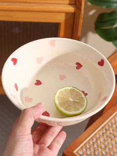 a hand holding a white bowl with a lime in it and hearts on the side