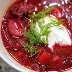 a white bowl filled with soup and sour cream on top of red sauce, garnished with green sprigs