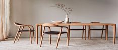 a wooden table with four chairs and a vase on top of it in front of a white wall