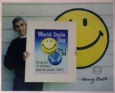 a man holding up a sign with a smiley face on it and the words world smile day