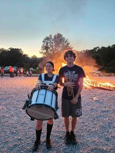 two people standing next to each other holding musical instruments in front of a fire pit