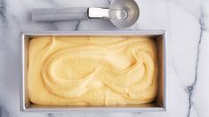 a pan filled with yellow batter on top of a marble counter next to a measuring spoon