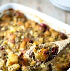 a wooden spoon in a casserole dish filled with stuffing and cranberries