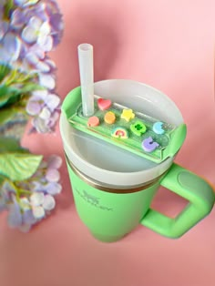 a green cup filled with buttons on top of a pink surface next to purple flowers