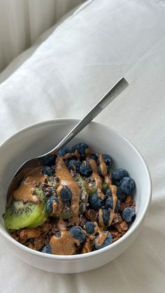 a bowl filled with cereal and blueberries on top of a white table cloth next to a spoon