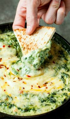 a hand dipping a tortilla chip into a bowl of spinach and cheese