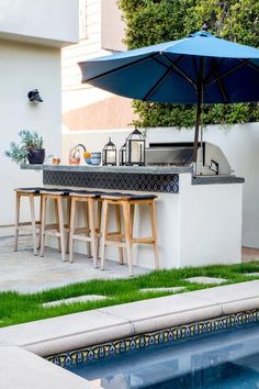 an outdoor kitchen with bar stools next to a swimming pool and green grass on the ground