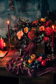 an arrangement of flowers, fruit and candles on a table