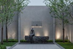 an outdoor fountain with trees and bushes in the foreground, surrounded by concrete walls