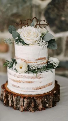 a wedding cake with white flowers and greenery is on top of a tree stump