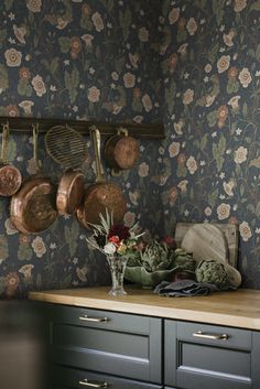 pots and pans are hanging on the wall next to a kitchen counter with flowers