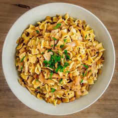 a white bowl filled with pasta and parsley on top of a wooden table next to a fork