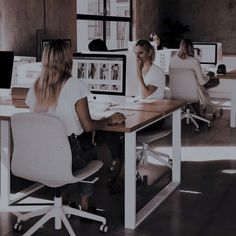 two women sitting at desks in an office setting with computers on each side of the desk