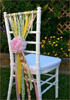 a white chair with a flower and ribbon tied to it's back, sitting in the grass