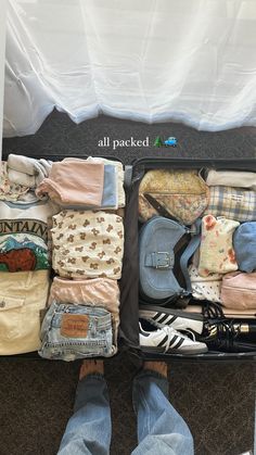 an open suitcase filled with clothes on the floor next to a person's feet