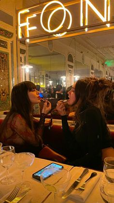 two women sitting at a table in front of a neon sign that reads f o n