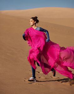 a woman in a pink dress is running through the desert