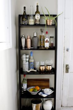 a shelf filled with lots of bottles and glasses next to a white door in a room