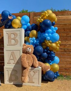 a teddy bear sitting on top of blocks with balloons in the background and a person standing next to it