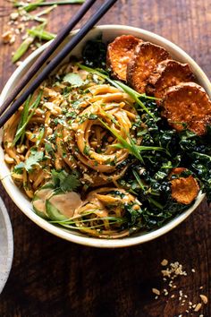 a bowl filled with noodles and vegetables next to chopsticks on a wooden table