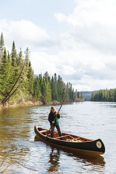 a man in a canoe paddling on the water with trees and sky behind him