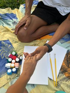 two people sitting on a blanket holding hands with paint and pencils next to each other