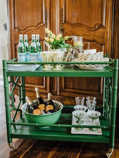 a green bar cart filled with bottles and glasses