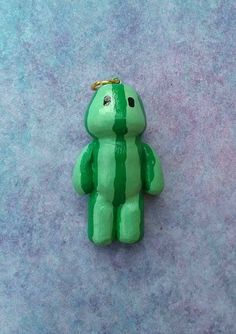 a small green teddy bear sitting on top of a purple floor next to a blue wall