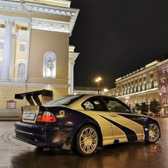 a black and yellow car parked in front of a large building at night with lights on