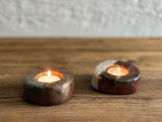 two small candles sitting on top of a wooden table next to each other with one burning