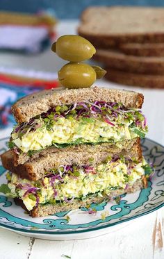 an egg salad sandwich is stacked high on a plate with olives and lettuce