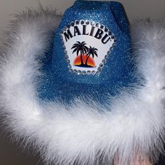 This is a Malibu Rum inspired hat with blue glitter and a white feather boa. The colors are not customizable as the hat is already made and ready to ship! If you are looking for something custom, I have a separate custom hat listing for that available. Sizing: The hat is an adult size hat that is 5 inches tall and 25 inches in circumference. It is designed to be a "one size fits all" hat meaning that if your head is on the smaller side, the hat may be larger on you. Slightly smaller hats are ava Malibu Cowgirl Hat, White Feather Boa, Malibu Rum, Personalized Hats, Cowboy Party, White Feathers, Beach Hat, Cowgirl Hats, Costume Hats