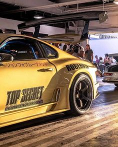 a yellow sports car parked in a garage with people looking at the cars on display