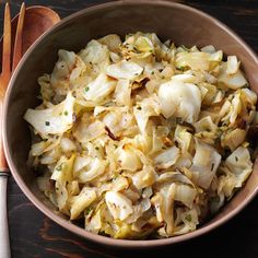 a wooden bowl filled with chopped onions next to two spoons and a fork on top of a table