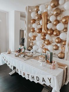 a birthday party with balloons and decorations on the wall behind a long table that is covered in white linens