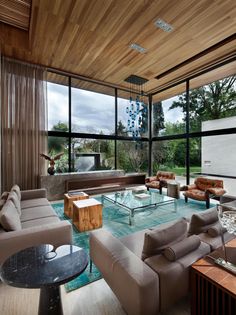 a living room filled with lots of furniture next to large glass windows on top of a wooden ceiling