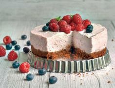 a cheesecake with berries and blueberries on a white wooden table next to it