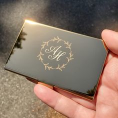 a person holding up a black and gold business card case with the letter h on it