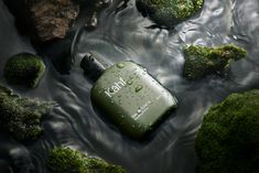 a bottle that is sitting in the water next to some rocks and mossy plants