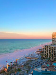 an aerial view of the beach and ocean at sunset, with hotels in the background