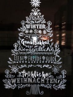 a lighted christmas tree in the window with words written on it and an image of a snowflake