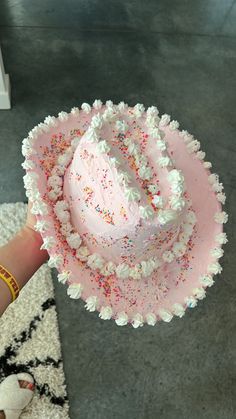 a pink cake with sprinkles on it being held by someone's hand