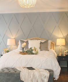 an instagram photo of a bedroom with white bedding and gray pillows, along with two lamps on either side of the bed