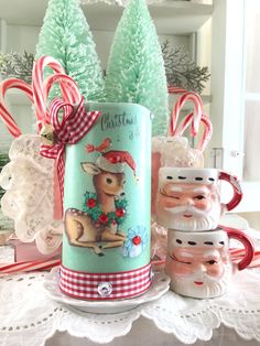 two christmas mugs sitting on top of a table next to some candy canes