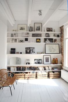 a white room with shelves filled with books and pictures on the wall next to a chair