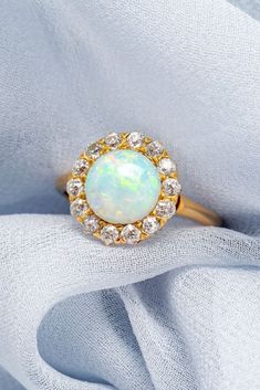 an opal and diamond ring sits atop a white cloth, surrounded by small diamonds