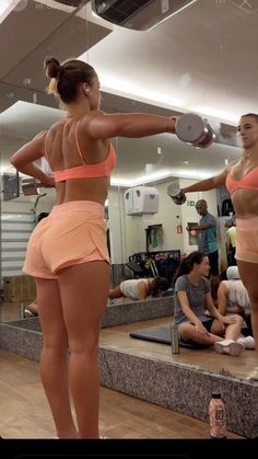 two women in sports bras and shorts are doing exercises with dumbbells while others look on