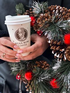 a woman's hands holding a coffee cup in front of pine cones and christmas decorations