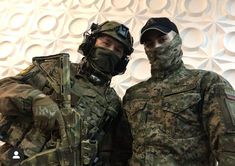 two men in camouflage gear standing next to each other with their arms around one another